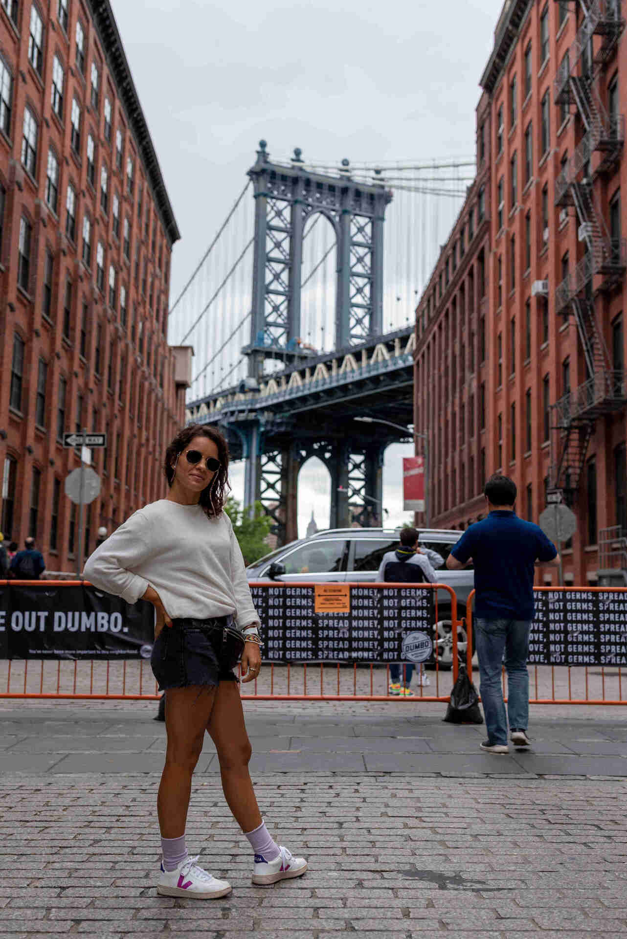 A woman in shorts and sneakers standing in front of a bridge in New York, enjoying the scenic view.